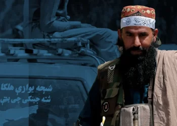 A Taliban member in a camouflage vest stands in front of a vehicle carrying armed men. (Photo Credit: AFP)
