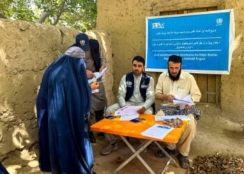 Two UN-Habitat workers write on a document as a woman in a burqa stands in front of them (Photo: UN-Habitat)