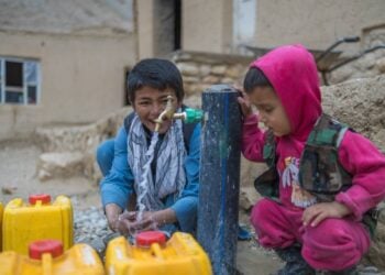 Two children collect water in yellow containers from a tap in a vulnerable area of Ghor. (Photo credit: UNICEF)