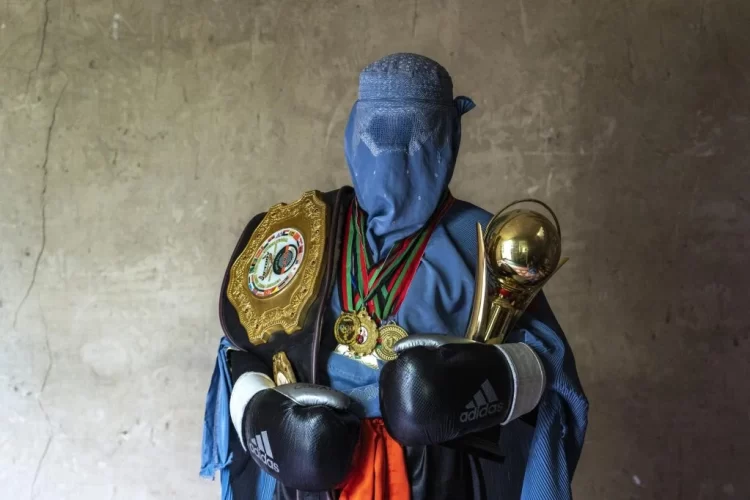 A woman in a burqa stands with medals, boxing gloves and a championship cup, highlighting women’s achievements in sports. (Photo credit: AP Photo/Ebrahim Noroozi)