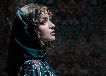 A woman in a headscarf looks upward, her face illuminated against a dark, patterned background (Photo: Pexels)