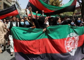 Protesters, including women wearing face masks, raise their fists and hold Afghanistan’s national flags during a rally on a city street. (Photo credit: Reuters / Stringer)