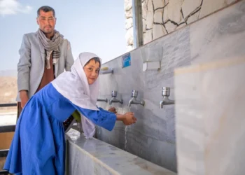 A girl washes her hands with tap water as a man stands behind her, highlighting efforts to improve access to safe drinking water in Afghanistan. (Photo credit: UNICEF)