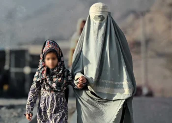 A woman in a burqa holds the hand of a young girl as they walk along a road in Afghanistan, where women heading households face poverty and social pressure. (Photo credit: AFP)