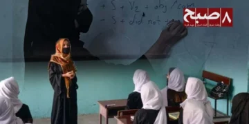 A female teacher in a face mask stands before schoolgirls in a classroom as restrictions on girls' education raise fears of a looming teacher shortage in Afghanistan. (Photo credit: 8am.media)