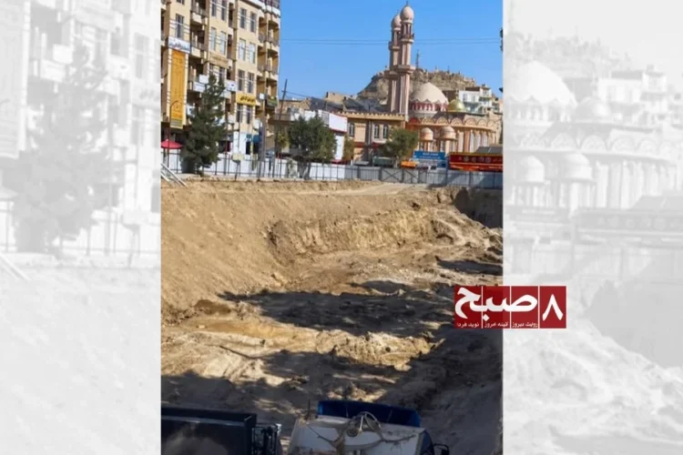 An excavation site for the underground market project in Ghazni city, with mounds of soil piled near commercial buildings and a mosque in the background. (Photo credit: 8am.media)