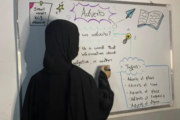 A girl writes an English lesson on adverbs on a whiteboard as students at Behdukht Online Academy teach one another. (Photo credit: Exclusive)