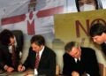 Officials sign a peace agreement beside a Northern Ireland flag and a protest sign in a composite image marking the Good Friday Agreement. (Photo credit: Social Media)