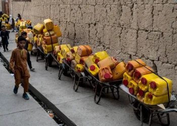 Boys walk past wheelbarrows loaded with yellow water containers along a mud-walled street in Kabul amid a worsening water crisis. (Photo credit: AFP)