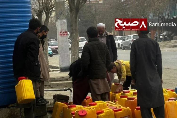 Men and boys gather around a public tap with rows of yellow jerrycans to collect water amid severe shortages in Kabul. (Photo credit: 8am.media)