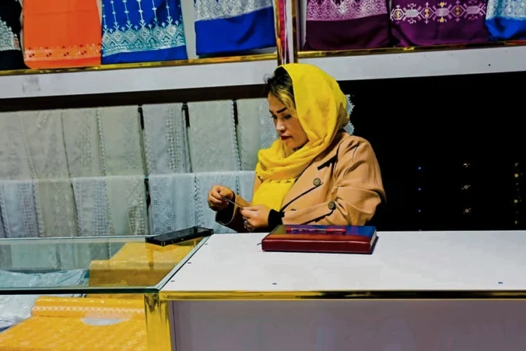 A woman entrepreneur sits behind the counter of her embroidered fabric shop in Kabul as businesses struggle amid rising costs and falling sales. (Photo credit: Exclusive)