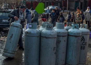 A man rolls a liquefied gas cylinder as residents gather around rows of LPG cylinders in the cold amid rising fuel prices. (Photo credit: AFP)