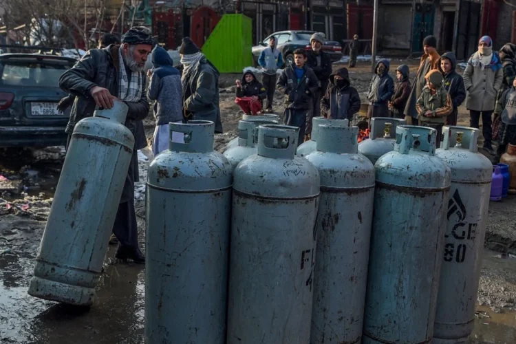 A man rolls a liquefied gas cylinder as residents gather around rows of LPG cylinders in the cold amid rising fuel prices. (Photo credit: AFP)