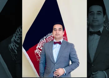 Nazifullah Salarzai, wearing a gray suit and burgundy bow tie, stands in front of an Afghanistan flag. (Photo credit: Exclusive)