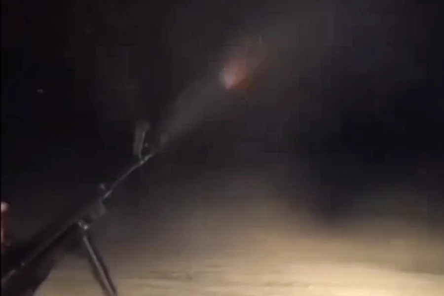 A still from a social media video shows a tripod-mounted machine gun firing at night, with a muzzle flash lighting the dark. (Photo credit: social media)