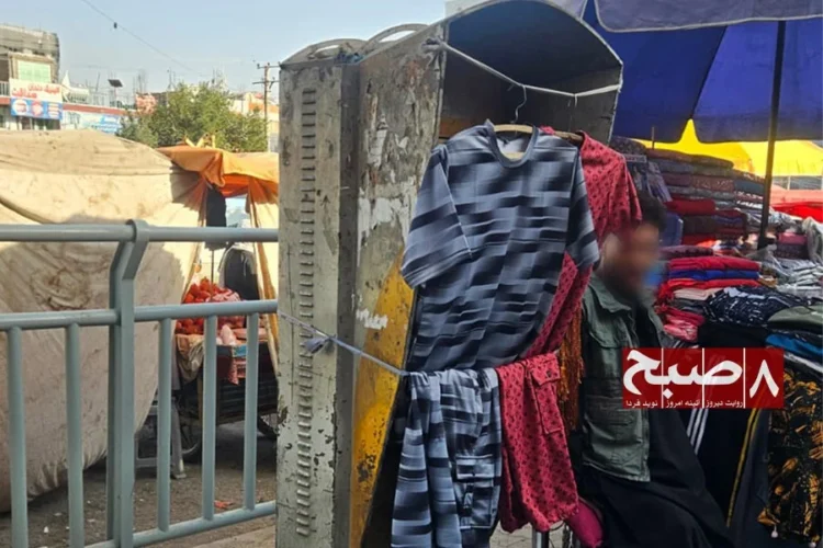 A street vendor displays clothes hung on a worn metal cabinet at a crowded roadside market stall. (Photo credit: 8am.media)