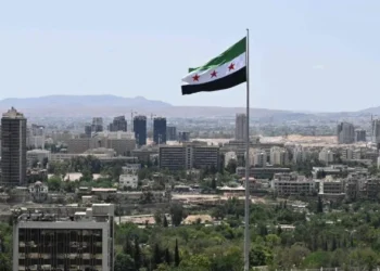Syrian flag flying high in the wind as the city’s infrastructure is seen in the background (Photo: AFP)