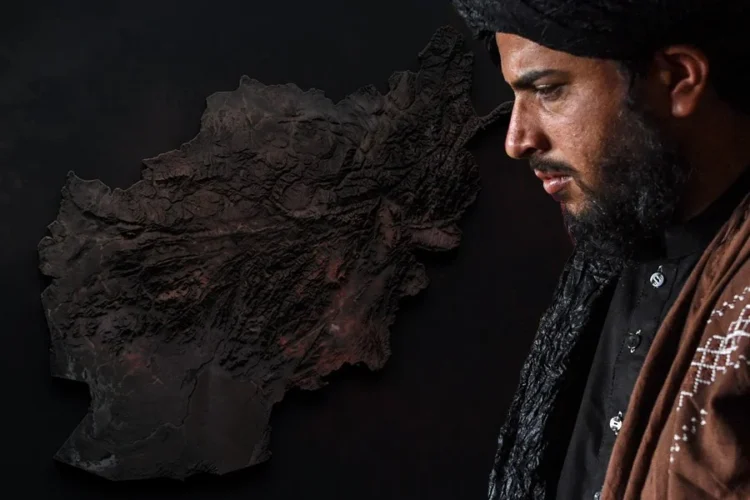 A Taliban fighter stands against a backdrop featuring a map of Afghanistan. (Photo credit: AFP)