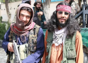 Two armed Taliban fighters, one holding a rifle, pose for a photo near a military vehicle as a 2026 US report accuses the group of continued abuse of children. (Photo credit: Social Media)