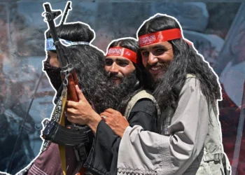 Three smiling Taliban members in red headbands stand close together, one of them carrying a rifle, as opposition to the group’s rule grows. (Photo credit: AFP)