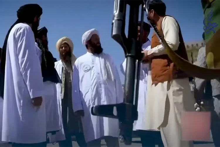 Taliban officials in white robes stand around a mounted rifle during a gathering. (Photo credit: social media)