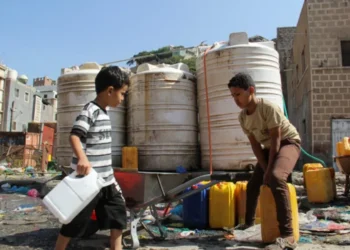 Two young boys collect water in plastic containers near large water storage tanks (Photo: Reuters) 