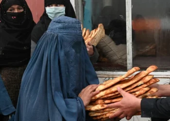 A woman in a blue burqa receiving bread (Photo: AFP)