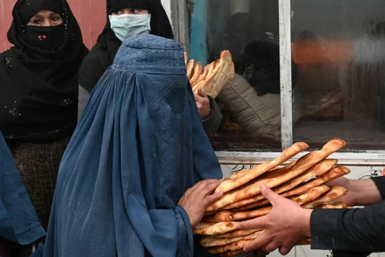 A woman in a blue burqa receiving bread (Photo: AFP)