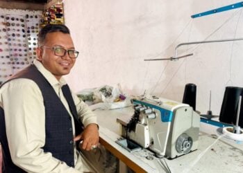 An Afghan returnee sitting in front of a sewing machine and smiling for the camera (Photo: UNHCR)
