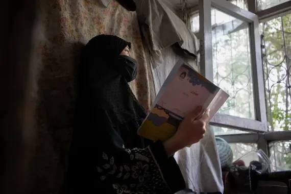 An Afghan girl holding her book and standing in front of a window (Photo: UNICEF)