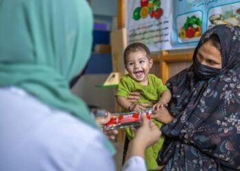 A female doctor gives a biscuit to a child held by their mother amid rising malnutrition among children in Afghanistan. (Photo credit: UNICEF)