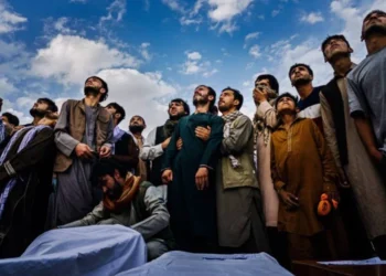 A crowd of people standing and looking up while there are several wrapped bodies (Photo: Getty Images)
