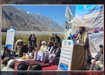 A Taliban official speaks at a podium as men sit on carpets during the inauguration of the Wakhan road in Badakhshan, with snow-capped mountains in the background. (Photo credit: FitratHamd)