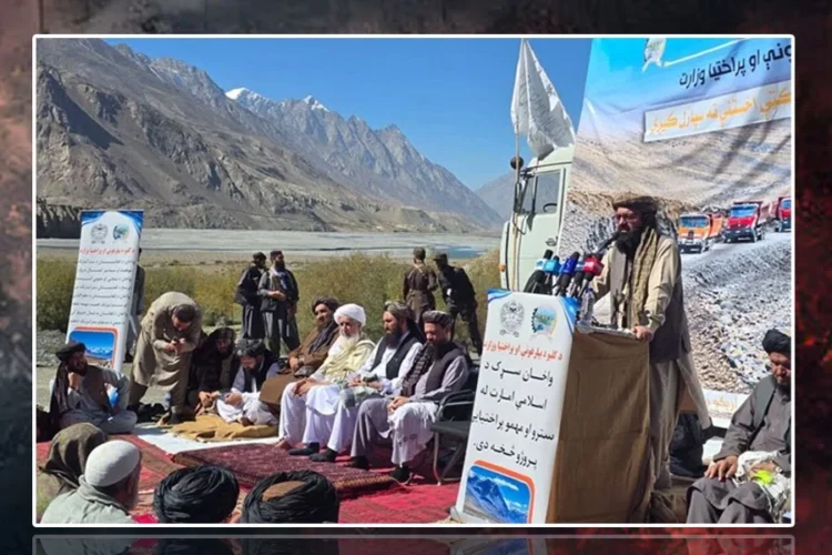A Taliban official speaks at a podium as men sit on carpets during the inauguration of the Wakhan road in Badakhshan, with snow-capped mountains in the background. (Photo credit: FitratHamd)