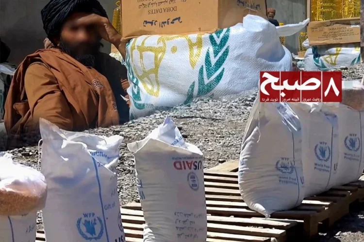 Sacks of WFP and USAID food aid are stacked on pallets as a man looks on in Zabul amid claims of Taliban interference in aid distribution. (Photo credit: 8am.media)