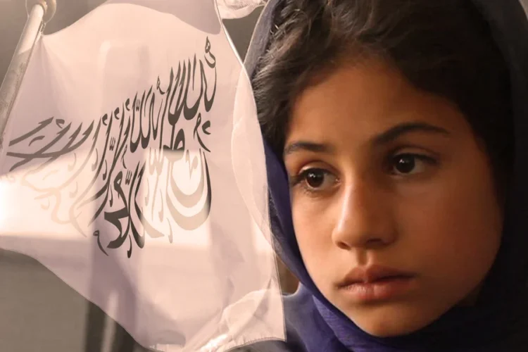 A young Afghan girl looks on with a serious expression, with the Taliban flag visible beside her (Photo: CNN)