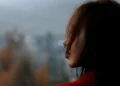 A young woman looks into the distance, her face partially hidden by her hair against a blurred city background (Photo: Pexels)