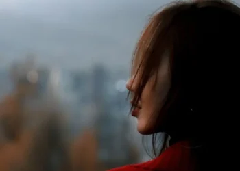 A young woman looks into the distance, her face partially hidden by her hair against a blurred city background (Photo: Pexels)
