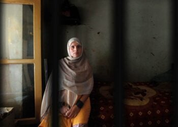 An Afghan woman wearing a headscarf sits quietly inside a dimly lit room (Photo: Gabriela Maj)
