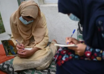 Two young Afghan girls sitting outside and writing in their notebooks (Photo: AFP)